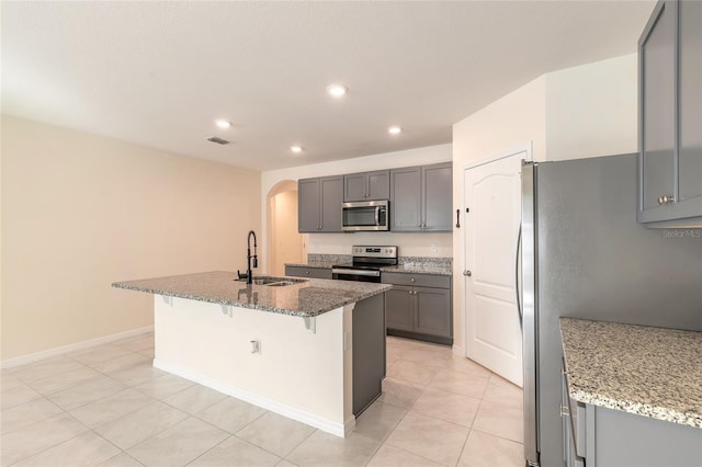 kitchen with a kitchen bar, stainless steel appliances, an island with sink, sink, and light stone counters