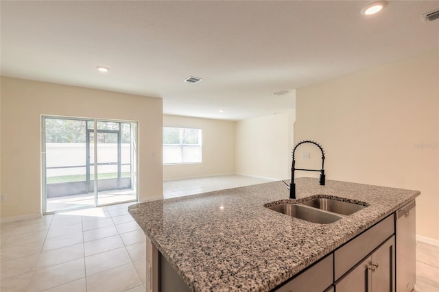 kitchen featuring stainless steel dishwasher, sink, a kitchen island with sink, light stone countertops, and light tile patterned floors