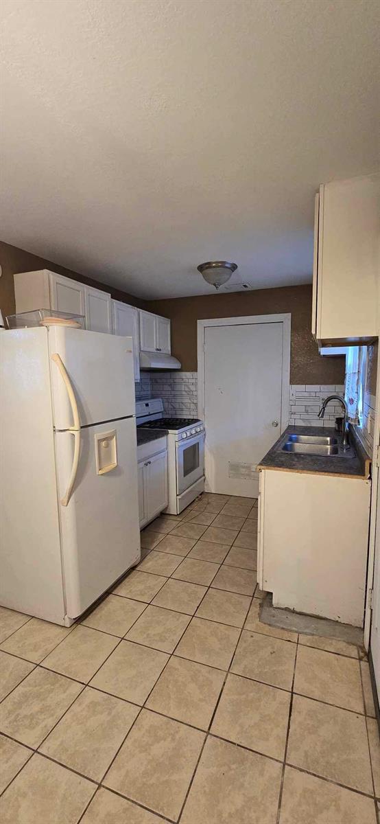 kitchen with white appliances, white cabinetry, decorative backsplash, sink, and light tile patterned floors