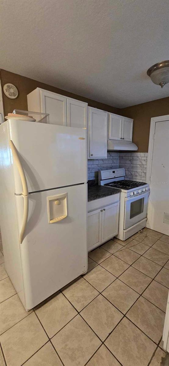 kitchen with light tile patterned floors, decorative backsplash, white appliances, a textured ceiling, and white cabinets