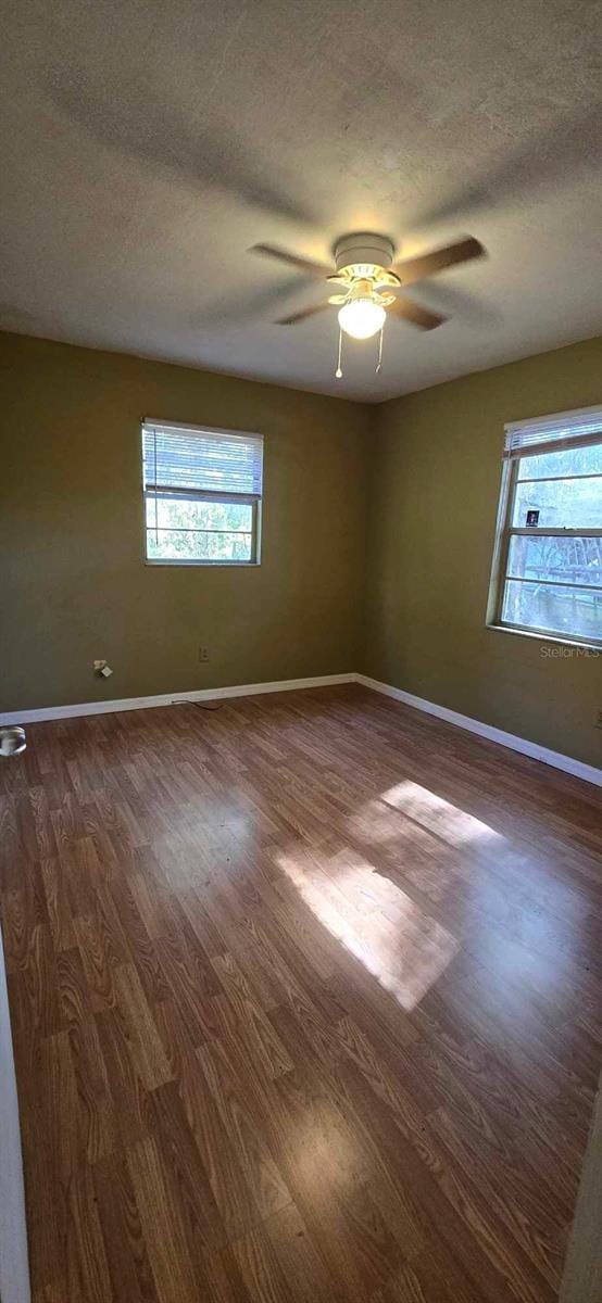 empty room with a textured ceiling, ceiling fan, and dark hardwood / wood-style floors