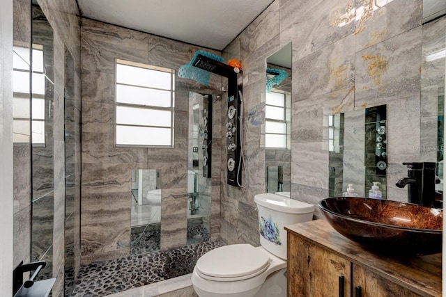 bathroom with toilet, vanity, tile walls, and a tile shower