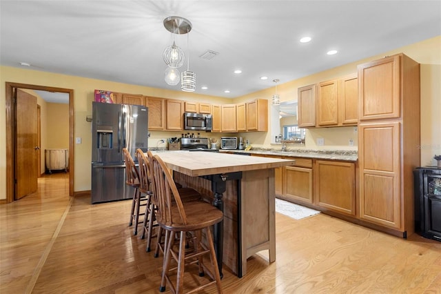 kitchen featuring a center island, pendant lighting, light wood-type flooring, stainless steel appliances, and light brown cabinetry