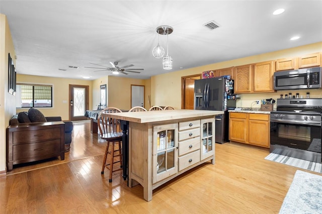 kitchen featuring a kitchen bar, appliances with stainless steel finishes, light wood-type flooring, hanging light fixtures, and a center island