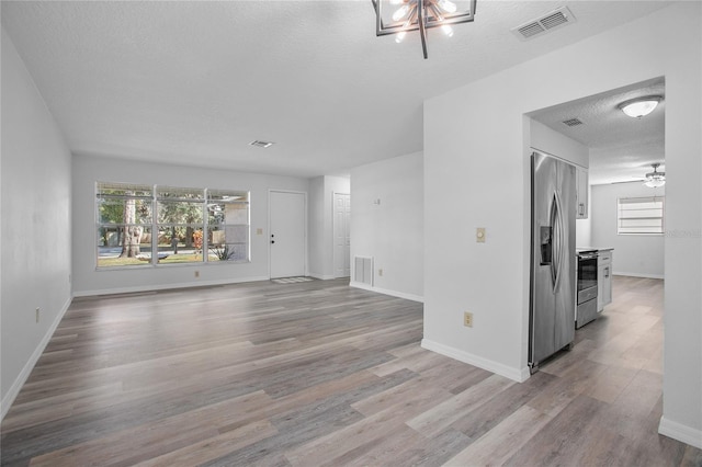 unfurnished living room with a textured ceiling, ceiling fan, and light hardwood / wood-style flooring