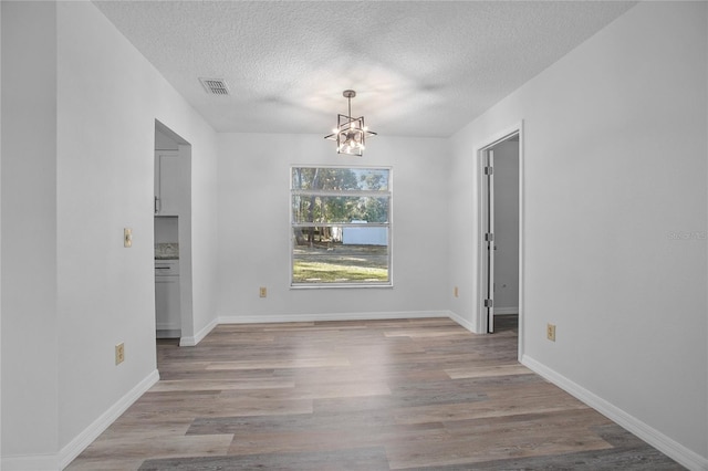 unfurnished dining area featuring a textured ceiling, light hardwood / wood-style floors, and a notable chandelier