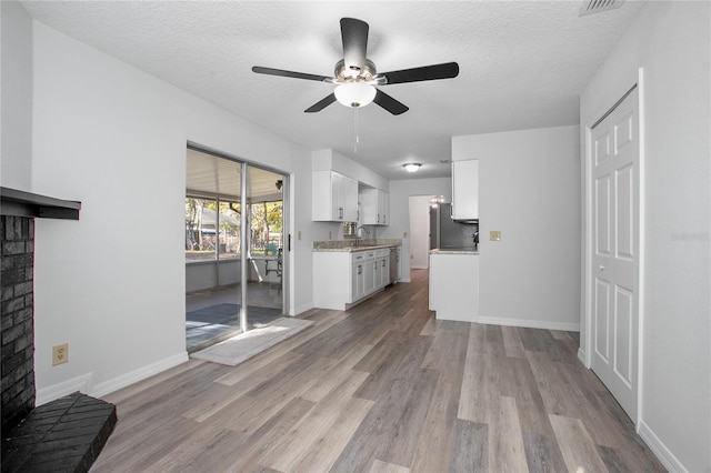 unfurnished living room with a textured ceiling, ceiling fan, light hardwood / wood-style flooring, and sink