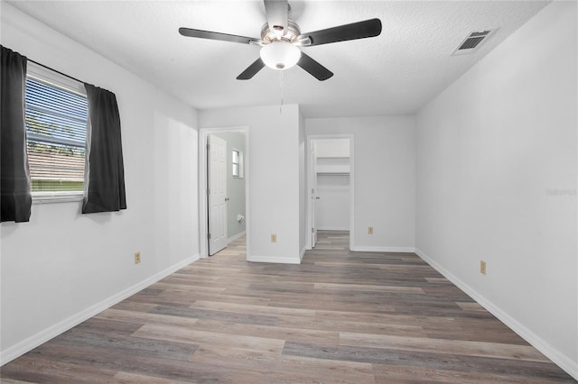 unfurnished bedroom featuring a textured ceiling, a walk in closet, hardwood / wood-style flooring, a closet, and ceiling fan