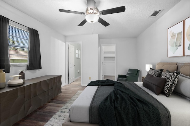 bedroom featuring hardwood / wood-style floors, a textured ceiling, a walk in closet, connected bathroom, and ceiling fan