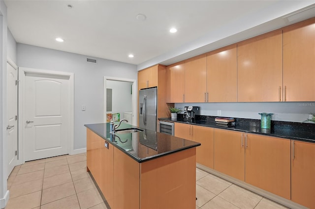 kitchen with sink, light tile patterned flooring, an island with sink, stainless steel fridge with ice dispenser, and dark stone counters