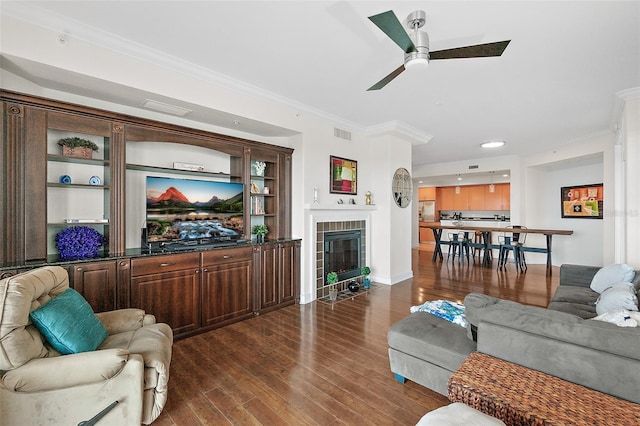 living room featuring a brick fireplace, dark hardwood / wood-style flooring, ornamental molding, and ceiling fan