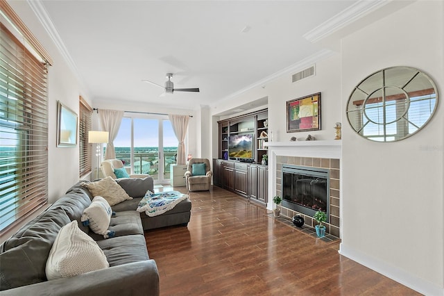 living room with ceiling fan, dark hardwood / wood-style floors, built in features, ornamental molding, and a tile fireplace