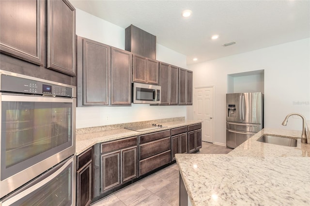 kitchen featuring stainless steel appliances, dark brown cabinets, light stone counters, and sink