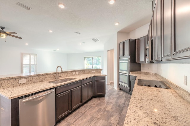 kitchen featuring ceiling fan, stainless steel appliances, dark brown cabinets, light stone counters, and sink