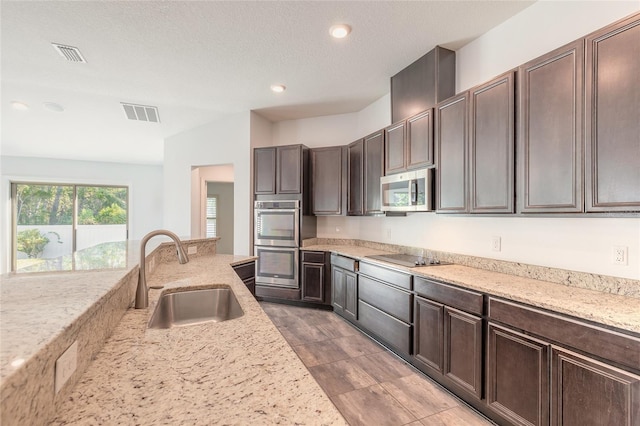 kitchen featuring sink, stainless steel appliances, a textured ceiling, dark brown cabinets, and light stone counters