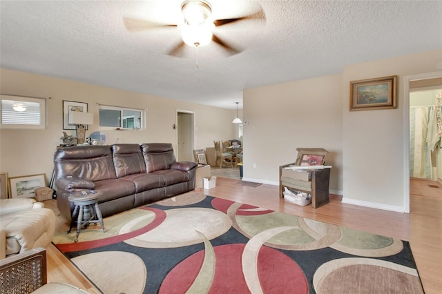 living room featuring light wood-type flooring, ceiling fan, and a textured ceiling