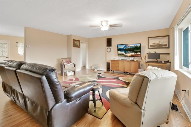 living room with a textured ceiling, ceiling fan, and light hardwood / wood-style flooring