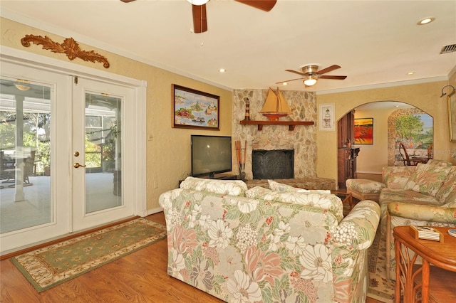 living room featuring crown molding, ceiling fan, hardwood / wood-style floors, a stone fireplace, and french doors