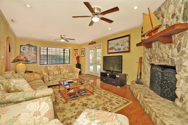 living room with a fireplace, wood-type flooring, ornamental molding, ceiling fan, and french doors