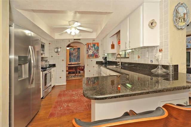 kitchen featuring white cabinetry, dark hardwood / wood-style floors, a raised ceiling, kitchen peninsula, and stainless steel appliances