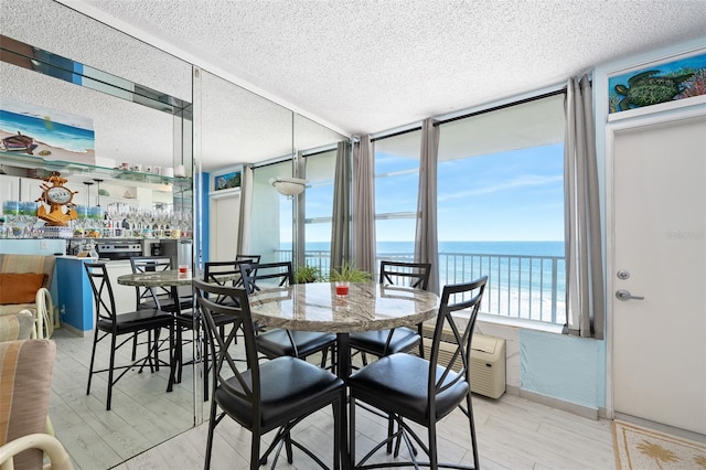 dining area featuring light wood-type flooring, a wall of windows, a textured ceiling, and a water view