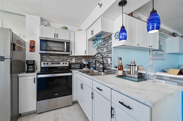 kitchen featuring white cabinetry, stainless steel appliances, backsplash, pendant lighting, and sink