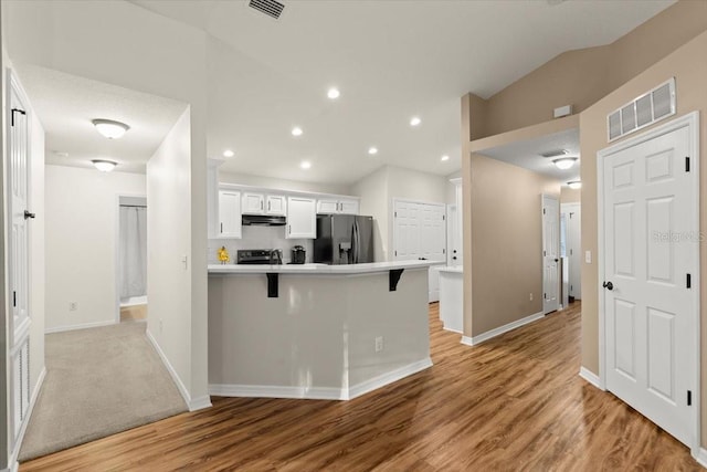 kitchen with a kitchen bar, white cabinetry, stainless steel refrigerator with ice dispenser, kitchen peninsula, and vaulted ceiling