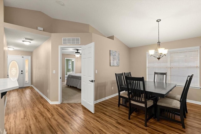 dining space featuring wood-type flooring, a chandelier, a textured ceiling, and vaulted ceiling