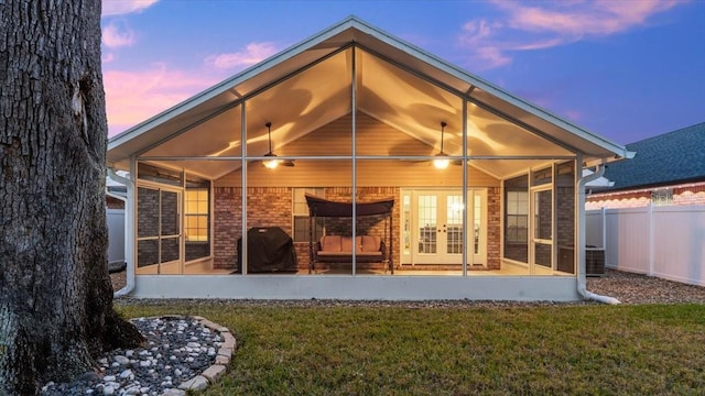 back house at dusk featuring a sunroom, a lawn, and french doors