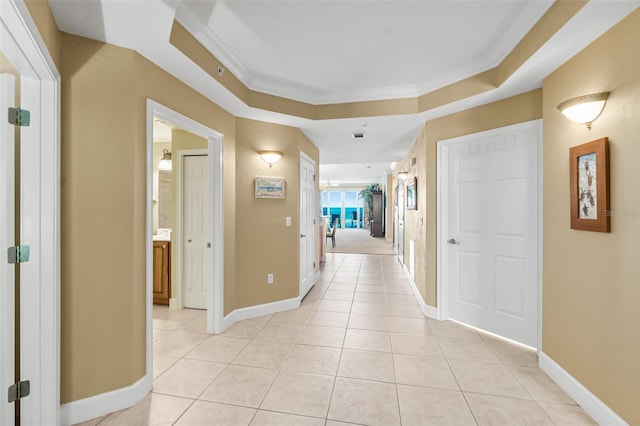 hallway with a tray ceiling, light tile patterned flooring, and crown molding