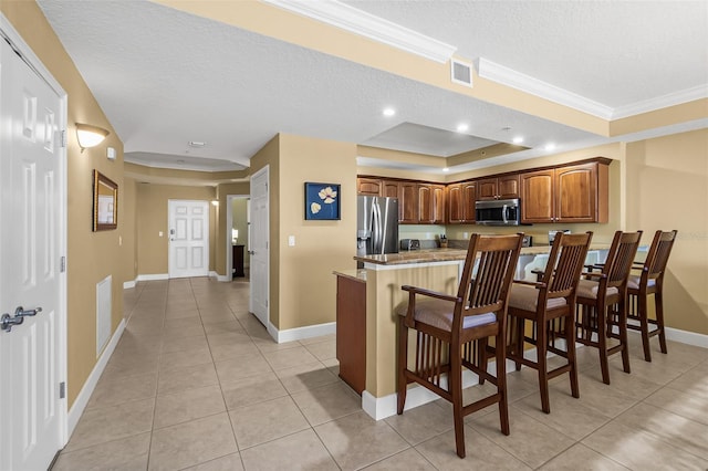 kitchen with a raised ceiling, appliances with stainless steel finishes, a breakfast bar area, a textured ceiling, and light tile patterned floors