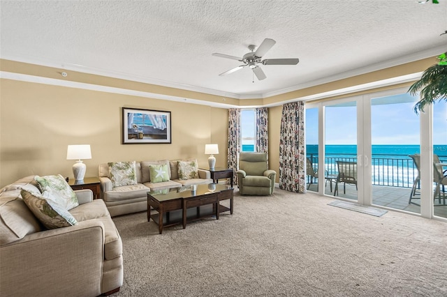 living room with a textured ceiling, carpet floors, ornamental molding, a water view, and ceiling fan