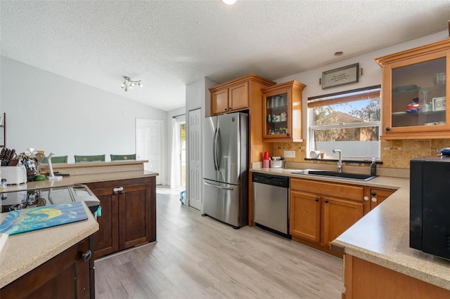 kitchen with sink, tasteful backsplash, light hardwood / wood-style flooring, a textured ceiling, and appliances with stainless steel finishes