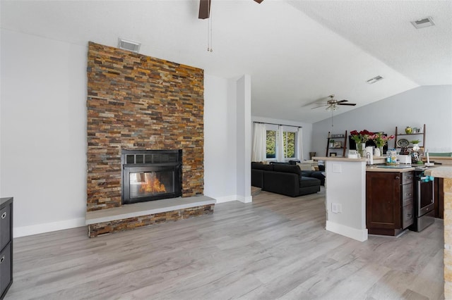 kitchen featuring dark brown cabinetry, vaulted ceiling, light hardwood / wood-style flooring, ceiling fan, and a fireplace