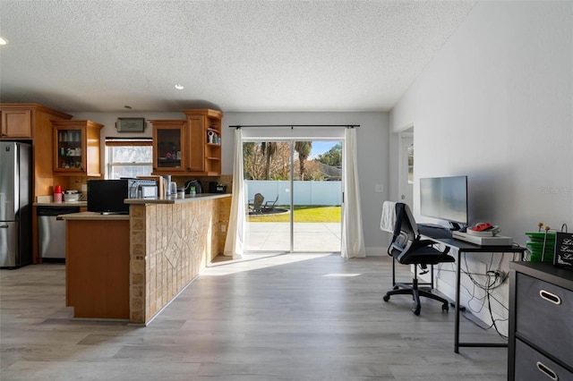 kitchen featuring a healthy amount of sunlight, stainless steel appliances, kitchen peninsula, and light wood-type flooring