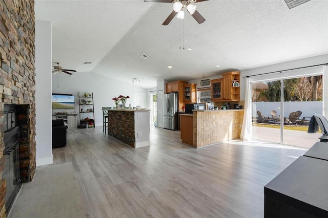 kitchen with a fireplace, stainless steel refrigerator, lofted ceiling, kitchen peninsula, and light wood-type flooring