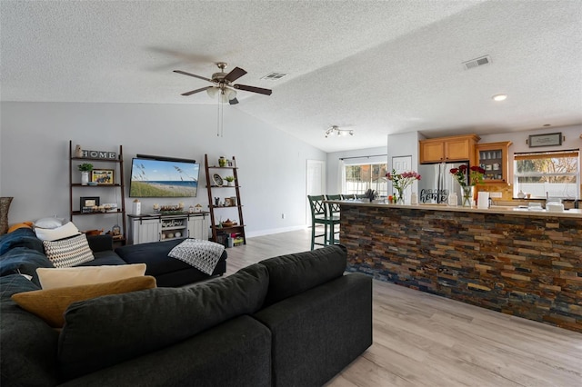 living room featuring vaulted ceiling, light hardwood / wood-style floors, and a textured ceiling