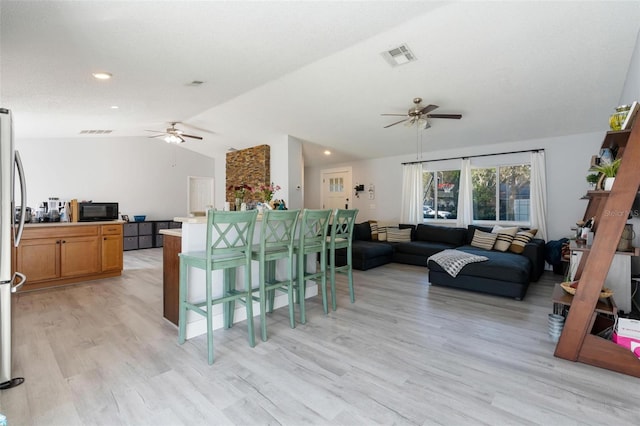 kitchen featuring ceiling fan, lofted ceiling, a kitchen breakfast bar, and light hardwood / wood-style flooring