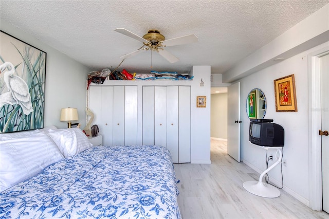 bedroom featuring ceiling fan, light wood-type flooring, a textured ceiling, and two closets