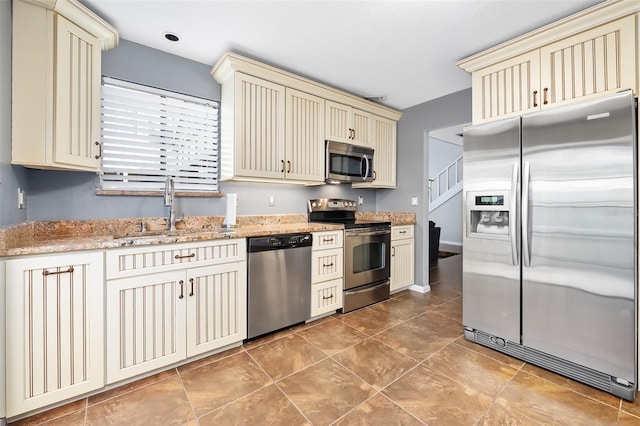 kitchen with sink, cream cabinets, light stone counters, and appliances with stainless steel finishes