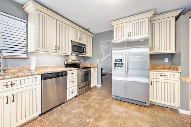 kitchen featuring light stone countertops, sink, appliances with stainless steel finishes, and cream cabinetry