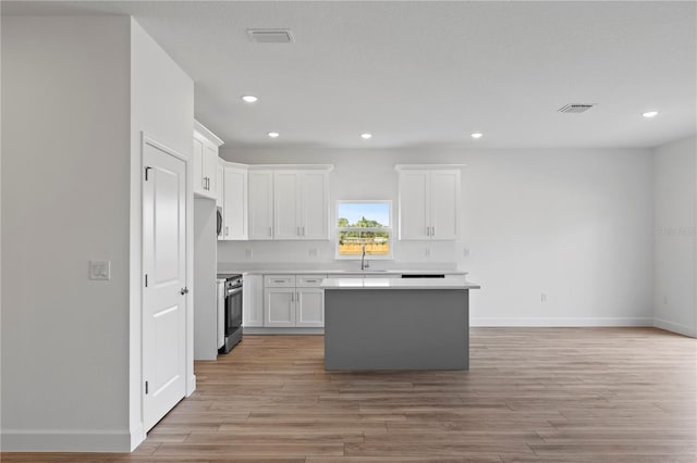 kitchen with a kitchen island, stainless steel electric stove, white cabinets, and sink