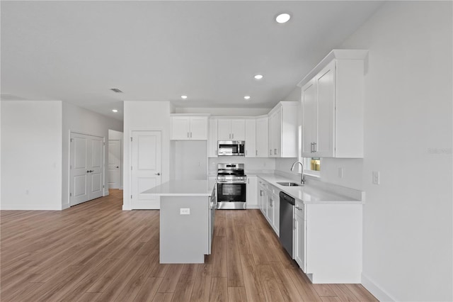 kitchen with light hardwood / wood-style flooring, sink, white cabinetry, a kitchen island, and stainless steel appliances