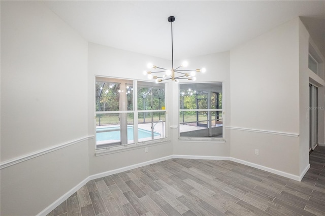 spare room featuring lofted ceiling, a notable chandelier, baseboards, and wood finished floors