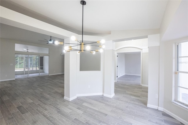 empty room featuring baseboards, arched walkways, wood finished floors, and ceiling fan with notable chandelier