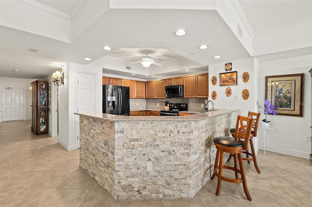 kitchen with sink, a tray ceiling, ornamental molding, black appliances, and kitchen peninsula