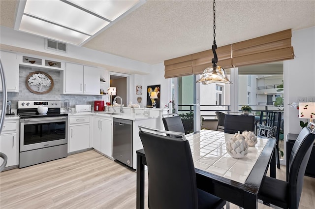 kitchen with sink, white cabinetry, decorative light fixtures, light hardwood / wood-style flooring, and stainless steel appliances