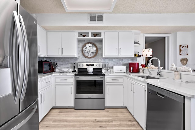 kitchen featuring sink, white cabinets, stainless steel appliances, light hardwood / wood-style floors, and backsplash