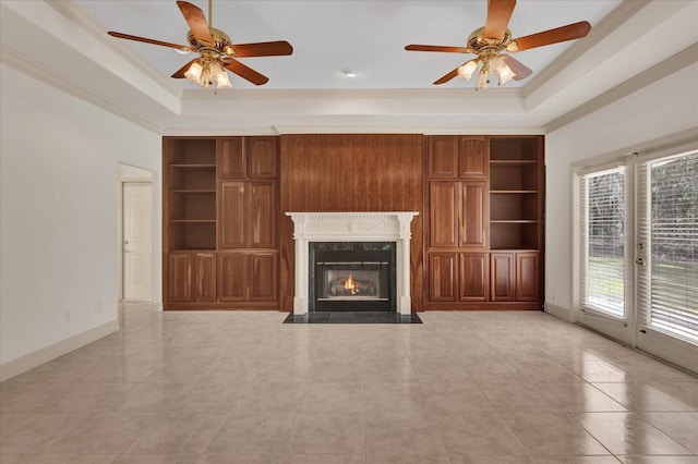 unfurnished living room with a raised ceiling, plenty of natural light, built in features, and a fireplace