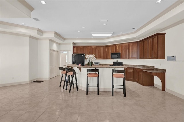 kitchen featuring an island with sink, a kitchen breakfast bar, black appliances, a raised ceiling, and crown molding